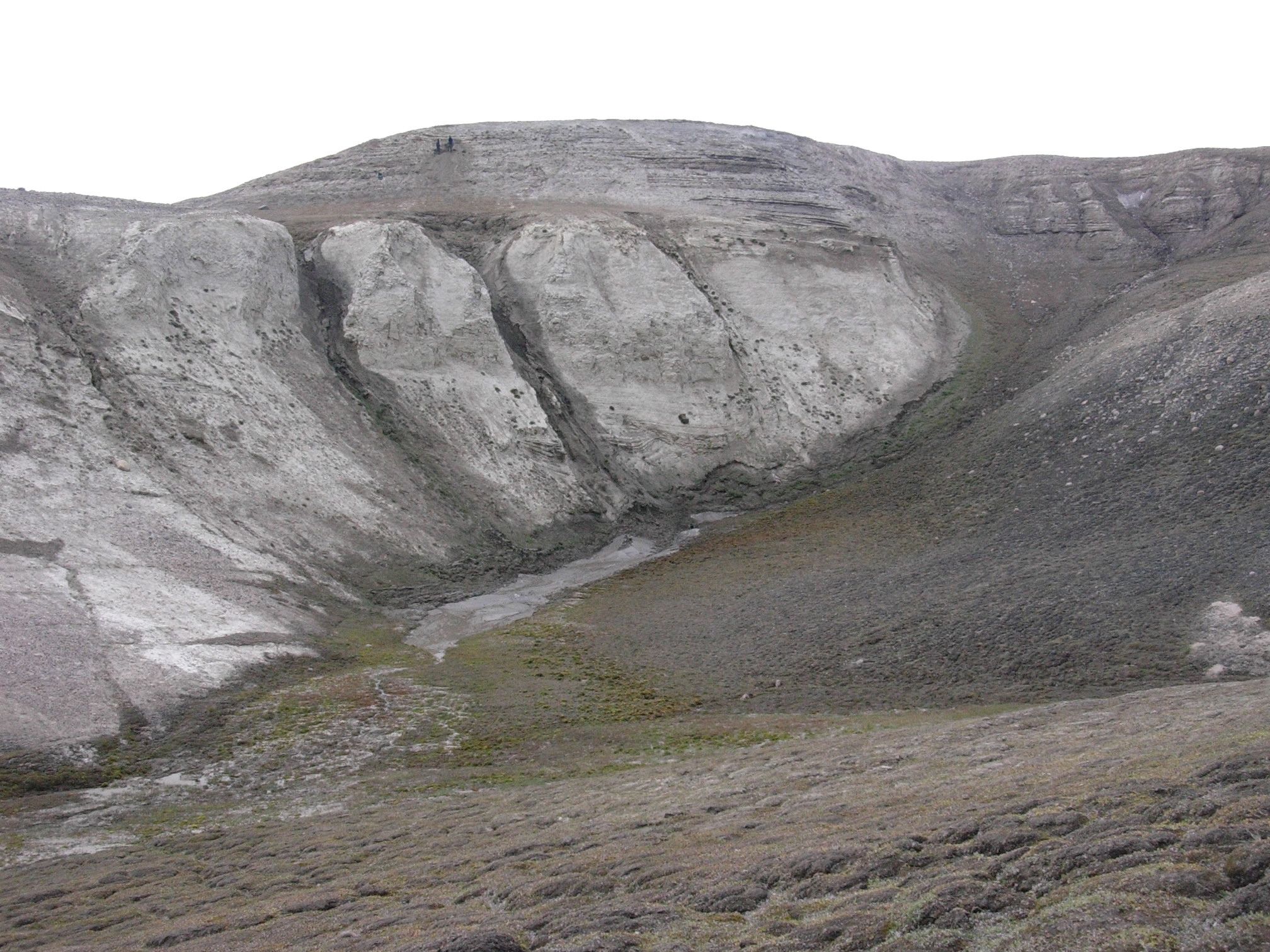 Hlavní lokalita v geologickém útvaru Kap K?benhavn. Mořské usazeniny jsou překryty pobřežními usazeninami jemného písčitého materiálu. Dvě osoby na vrcholu odebírají vzorky environmentální DNA.  Kredit: Svend Funder