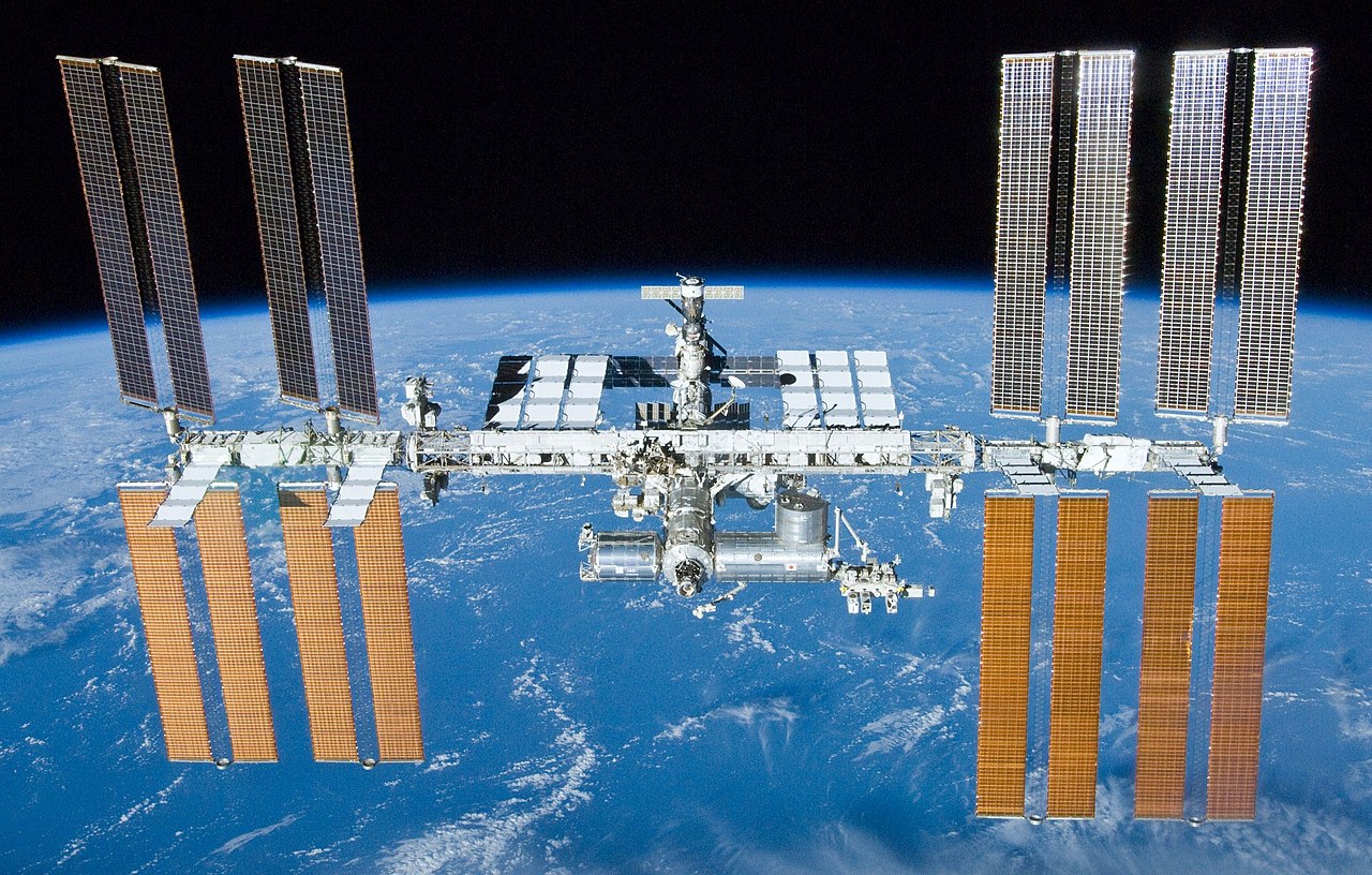 Medzinárodná vesmírna stanica ISS je už poriadny kolos- ale obývané sú len tie valce v strede obrázka. Americká časť je vpredu, ruská vzadu – nahor z nej čnie pripojený Sojuz. Wikipedia.