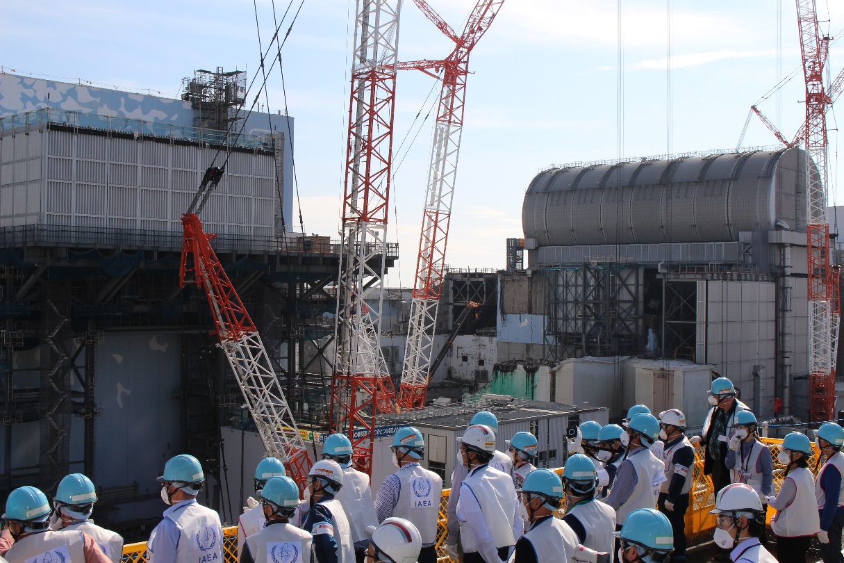 Inspekce týmu z Mezinárodní agentury pro atomovou energii, záběr na třetí blok připravený pro vyklízení palivových souborů a druhý blok s kontejnerem, který se využíván k průzkumu patra s bazénem s palivovými soubory (zdroj TEPCO).
