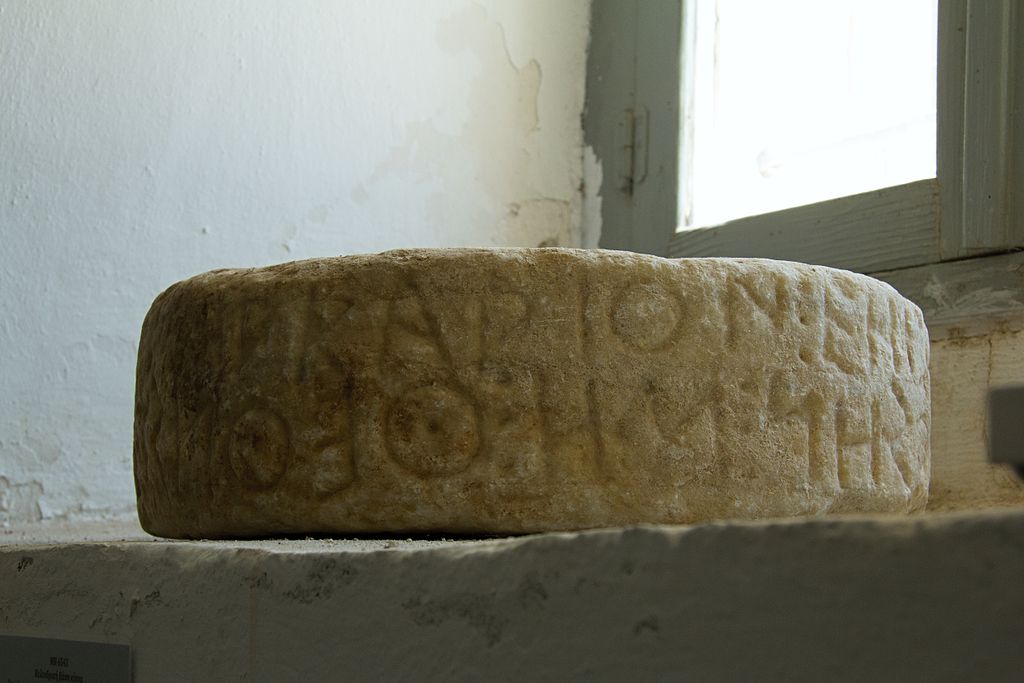 Base sloupu s cik-cak (bústrofédon) nápisem. Mramor, 42 x 11 cm. Archaická doba, závěr 6. století před n. l. Archeologické muzeum na Naxu (Chóra), MN 6543. Text nápisu? „Leukarión mě vytvořil jako pomník Theolista.“ - ????????? ????????? ?? ?????????