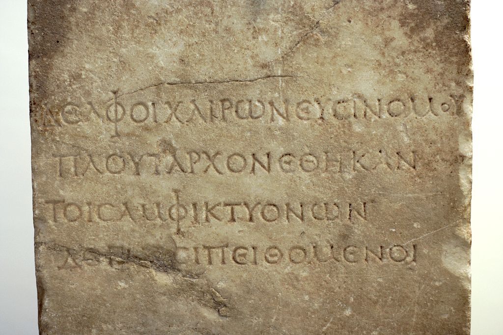 Pěkně čitelný řecký nápis z římské doby, kolem roku 100 n. l., tzv. Plútarchova stéla: „Delfští spolu s Chaironejskými věnovali tuto (Plútarchovu) podobu podle příkazu Amfiktyonie.“ Archeologické muzeum v Delfách, N 4070. Kredit: Zde, Wikimedia Commo
