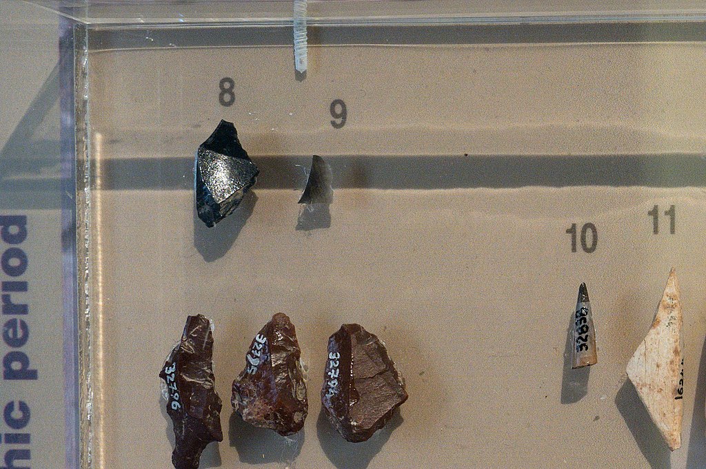 Vlevo nahoře jsou hroty z obsidiánu nalezené v jeskyni Franchthi, pod nimi pazourky. Obsidián přivezli z kykladského ostrova Mélu. Závěr paleolitu, 10 až 8 tisíc let před n. l. Archeologické muzeum v Naupliu. Kredit: Zde, Wikimedia Commons. Licence C