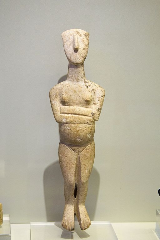 Stojící těhotná žena, mramor, 23 cm. Koumasa na Krétě, raná doba bronzová, 2700 až 2400 před n. l. Idol importovaný z Kyklad, varieta Spedos, kultura Keros-Syros. Archeologické muzeum v Irakliu, ?122. Kredit: Zde, Wikimedia Commons. Licence CC 4.0.