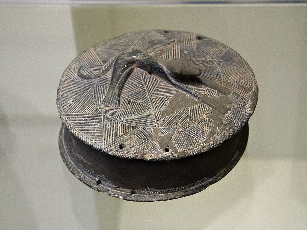 Pyxis s reliéfem ležícího psa na víčku. Chlorit nebo steatit, průměr 12,5 cm. Zakros, Údolí mrtvých. EM ??A, 2600 až 2300 před n. l. Archeologické muzeum v Irakliu, ?2719. Kredit: Zde, Wikimedia Commons. Licence CC 4.0.