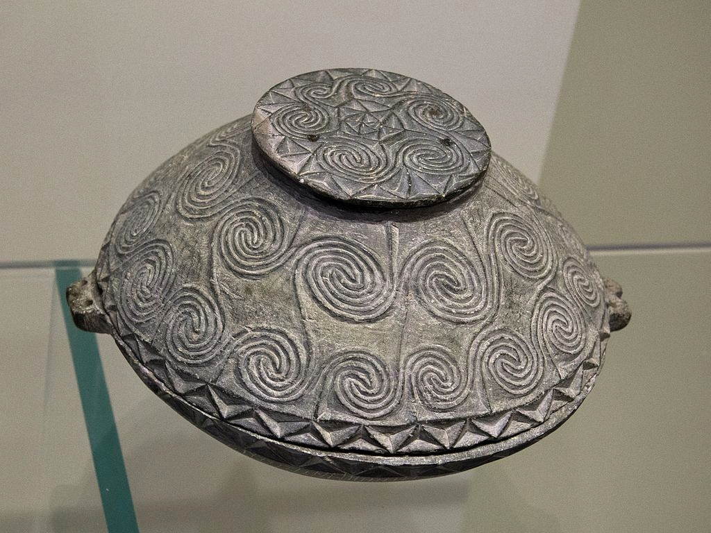 Pyxis s víčkem, s vyřezávaným reliéfem spirál. Chlorit, výška 11,85 cm. Nalezená u Maronie, okres Sitia. EM ???, 2600-2300 před n. l. Archeologické muzeum v Irakliu, ?2339. Kredit: Zde, Wikimedia Commons. Licence CC 4.0.
