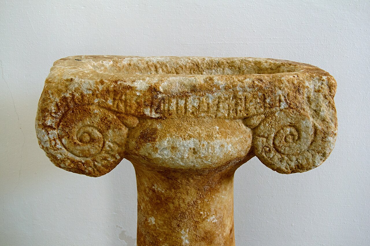 Jamka pro vkládání obětin na vrcholu sloupku, s nápisem, pozdní 7. století před n. l. Archeologické muzeum na Naxu, MN 8. Kredit: Zde, Wikimedia Commons. Licence CC 3.0.