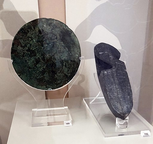Bronzový disk z Olympie, 6. až 5. stol. př. n. l. – a kamenné skokanské závaží z 5. stol. před n. l., nalezené v posvátném okrsku Olympie (Altis). Muzeum olympijských her v Olympii. Kredit: Davide Mauro, Wikimedia Commons. Licence CC 4.0.