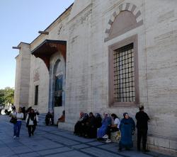 Pro ženy je do mešity vyčleněn malý postranní vchod. Při čekání na muže odpočívají na schodech, nebo kamenné zídce. Kredit: Osel