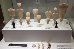 Mramorové figurky („idoly“) kykladského typu a další věci z pohřbů ve Fourni u Archanes na Krétě. „Idoly“ jsou z rané doby bronzové, snad kolem roku 2300 před n. l. a generace po něm. Archeologické muzeum v Irakliu, skříň 18. Kredit: Zde, Wikimedia Commons. Licence CC 4.0.