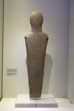Schematická kamenná figura, asi ženská postava, asi pod dojmem kykladských „idolů“, vysoká 67,5 cm. Nález ze Sambas Pediada, EM IIB až EM II, 2300 až 1900 před n. l. Archeologické muzeum v Irakliu, Γ1107. Kredit: Zde, Wikimedia Commons. Licence CC 4.0.