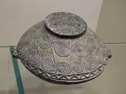 Pyxis s víčkem, s vyřezávaným reliéfem spirál. Chlorit, výška 11,85 cm. Nalezená u Maronie, okres Sitia. EM ΙΙΑ, 2600-2300 před n. l. Archeologické muzeum v Irakliu, Λ2339. Kredit: Zde, Wikimedia Commons. Licence CC 4.0.