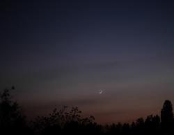 Zapadající srpek mladého Měsíce (je mu 43 hodin po novu) s Merkurem (vpravo) při začátku nautického soumraku, asi 7 stupňů nad obzorem, v květnu 2022. Disk Měsíce je doplněn popelavým svitem, tedy světlem Země. Vlevo dole je hvězdný obr Aldebaran. Kredit: Bautsch, Wikimedia Commons. Licence CC 1.0.