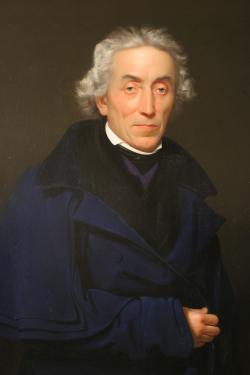 Josef Dobrovský (1753  – 1829). Kněz, filolog, historik. Zakladatel vědecké bohemistiky a slavistiky, čímž  předznamenal a podnítil české národní obrození. K jeho největším zásluhám patří zavedení a soustavné uplatňování kritické metody ve vědeckém bádání bez ohledu na dopad jeho výsledků. Byl jedním ze zakládajících členů Královské české společnosti nauk. S hrabětem Kašparem Šternberkem založil Vlastenecké (dnes Národní) muzeum. Po Husovi a Komenském je pokládán za třetího Čecha světového významu. Autorem olejomalby je Františka Tkadlíka. Zdroj: Národní muzeum. CC BY-SA 4.0