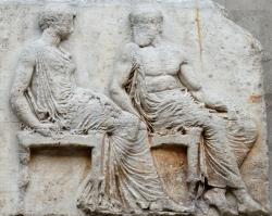 Athéna s kopím (které nyní chybí) sleduje průvod Velkých Panathénají. Héfaistos vedle ní se opírá o berlu. Blok V,36-37 z východního vlysu Parthenonu, 447-433 před n. l. British Museum. Kredit: Marie-Lan Nguyen, Wikimedia Commons. Licence CC 4.0.