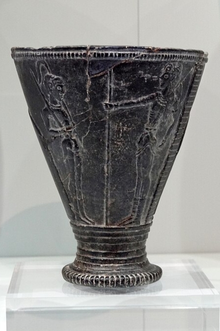 Kuželovitý pohár s reliéfem dvou postav. Dva mladíci odění jako důstojník (s mečem) a princ (s žezlem). Kréta, LM IA, 1550-1500 před n. l. Archeologické muzeum v Irakliu 341. Kredit: Olaf Tausch, Wikimedia Commons. Licence CC 3.0.