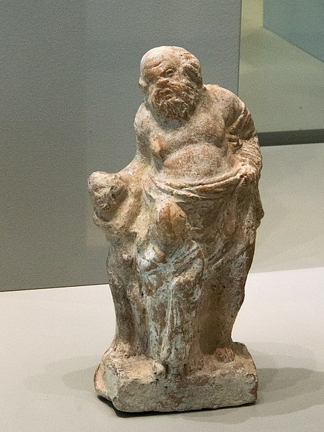 Pedagog se dvěma malými chlapci. Drobná terakota z Tanagry v Boiótii, 4. století před n. l. Altes Museum Berlin, TC 7084. Kredit: Zde, Wikimedia Commons.