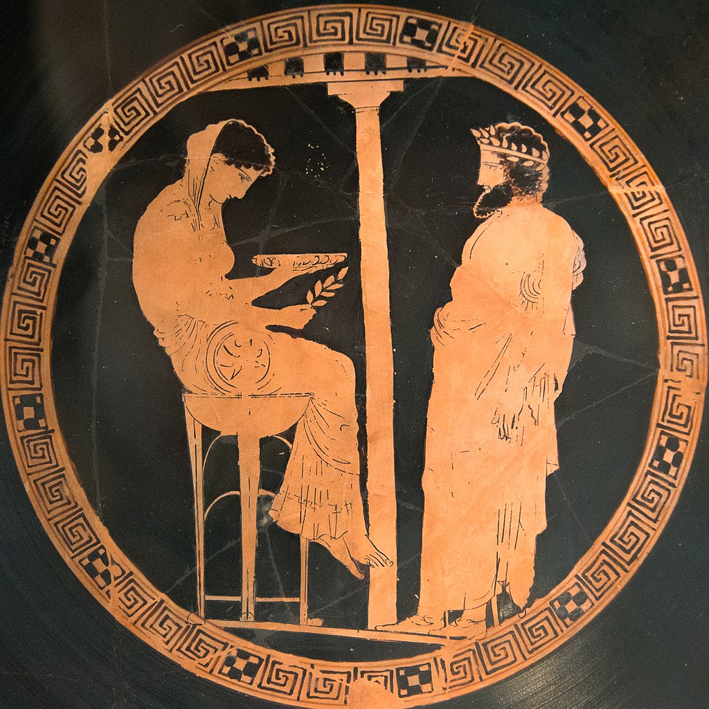 Attický červenofigurový kylix z Vulci (Itálie), 440-430 před n. l. Kodros Painter. Pythie nebo bohyně Métis věští králi Aigeovi. Podstatné teď je, že přitom sedí na vysoké trojnožce, kouká do misky a v pravé ruce drží snítku vavřínu. Berlin, Altes Mu