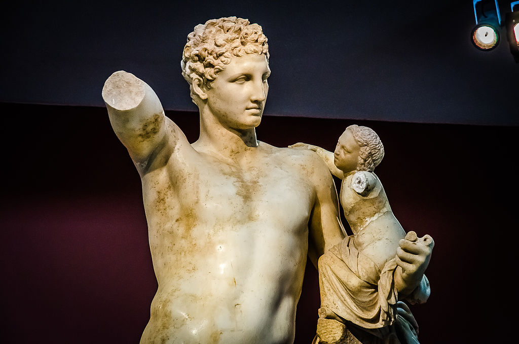 Hermés chová maličkého Dionýsa. Praxitelés, 350 až 330 před n. l. Archeologické muzeum v Olympii, ? 48. Kredit: Made by Numbers, Wikimedia Commons. Licence CC 2.0.